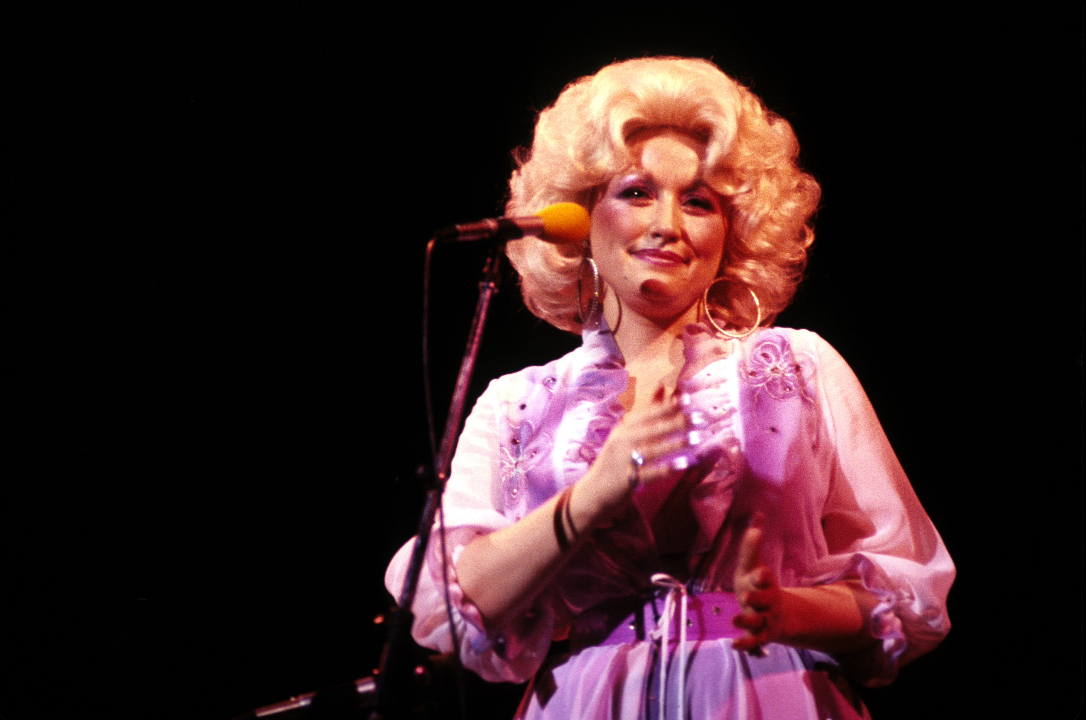 Dolly Parton on stage, speaking into a microphone.